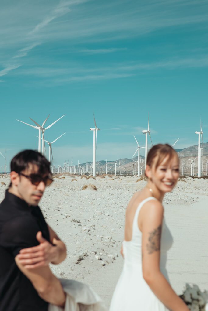Couple in front of the windmills in Palm Springs, California. The couple is dressed for a wedding and looking at the camera and smiling. 