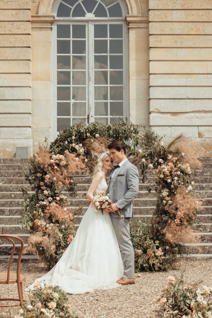 A bride and groom standing amidst the floral arc at the wedding venue Chateau de Champlatreux in France. 