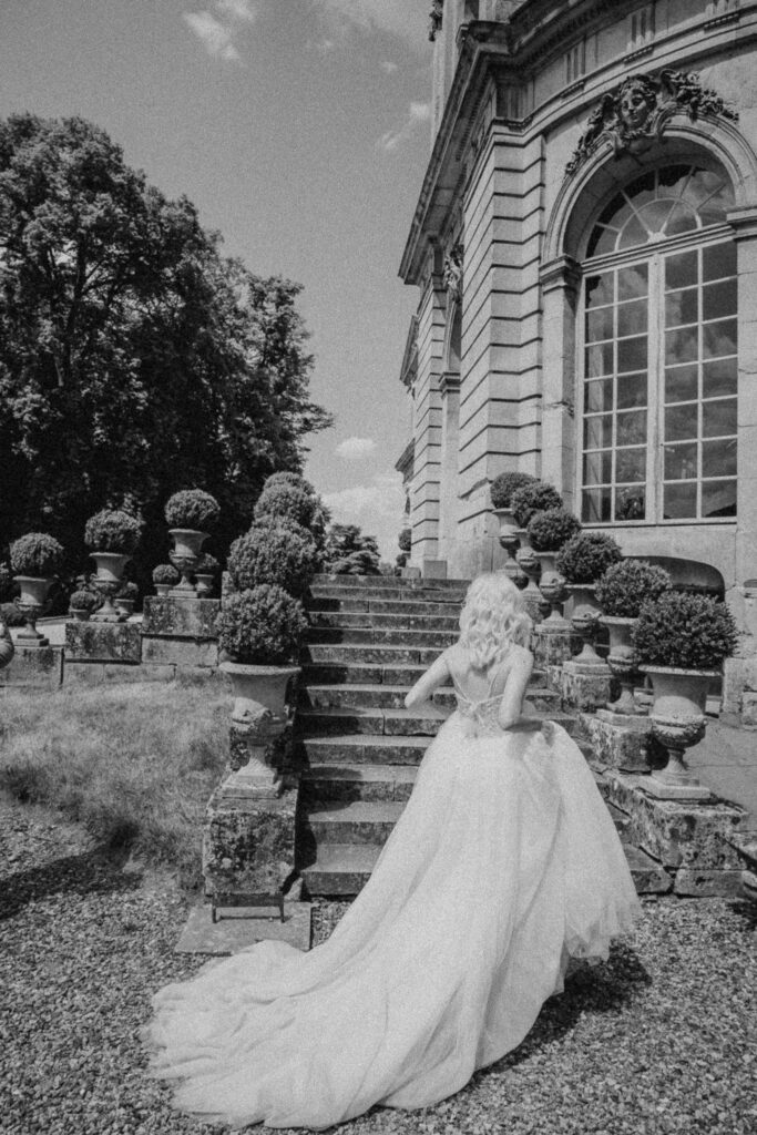 Bride holding her wedding dress as she begins to ascend the stairs at the wedding venue Chateau de Champlatreux in France. 
