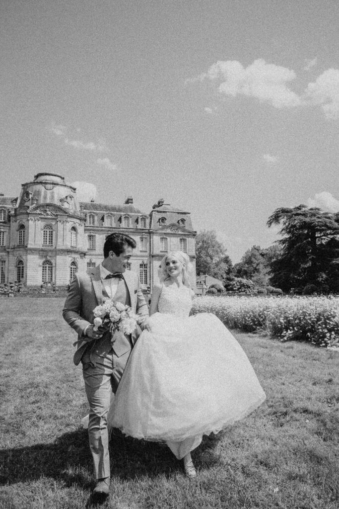 Bride and groom walking away from the wedding venue Chateau de Champlatreux in France. Black and white photograph. 