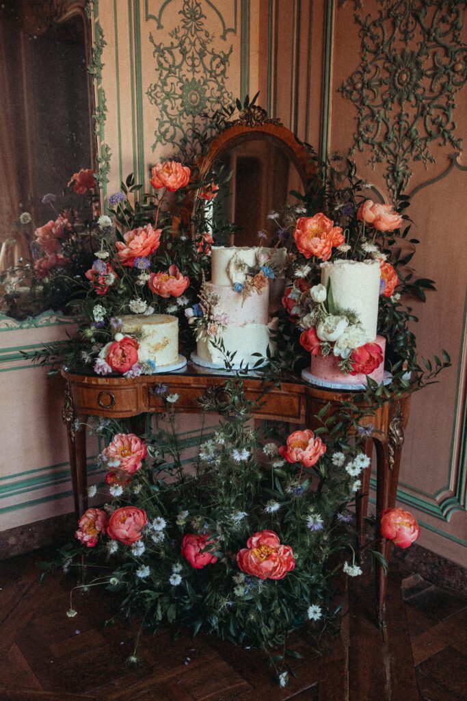 Antique vanity turned into a cake table, bedecked in flowers and cake at the wedding venue Chateau de Champlatreux in France. 