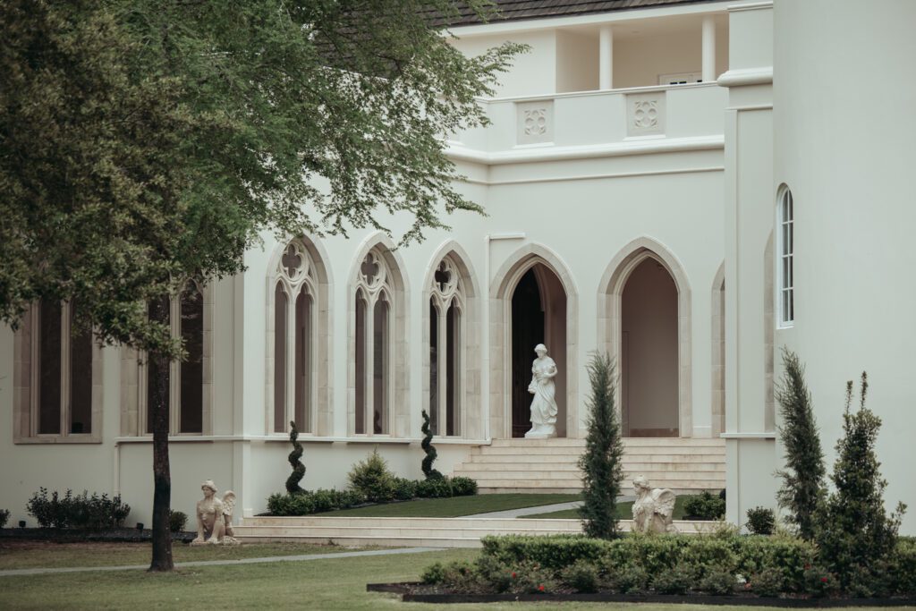 Picture of the exterior of Chateau Nouvelle in Houston, Texas. Stone archways and a statue and manicured lawns. 