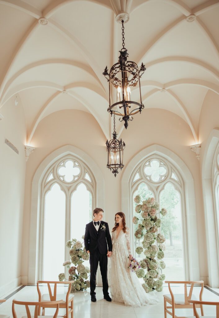 Bride and groom standing in the ceremony space inside of Chateau Nouvelle holding hands and looking at one another