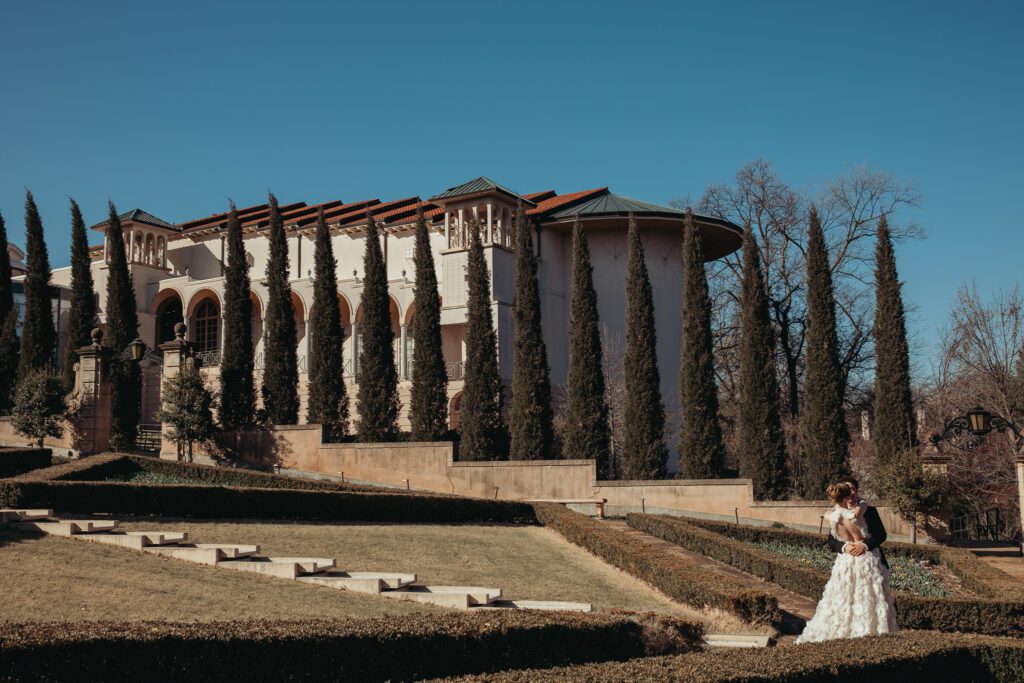 A couple on the grounds of The Philbrook Museum of Art surrounded by green lawns and tall trees. 