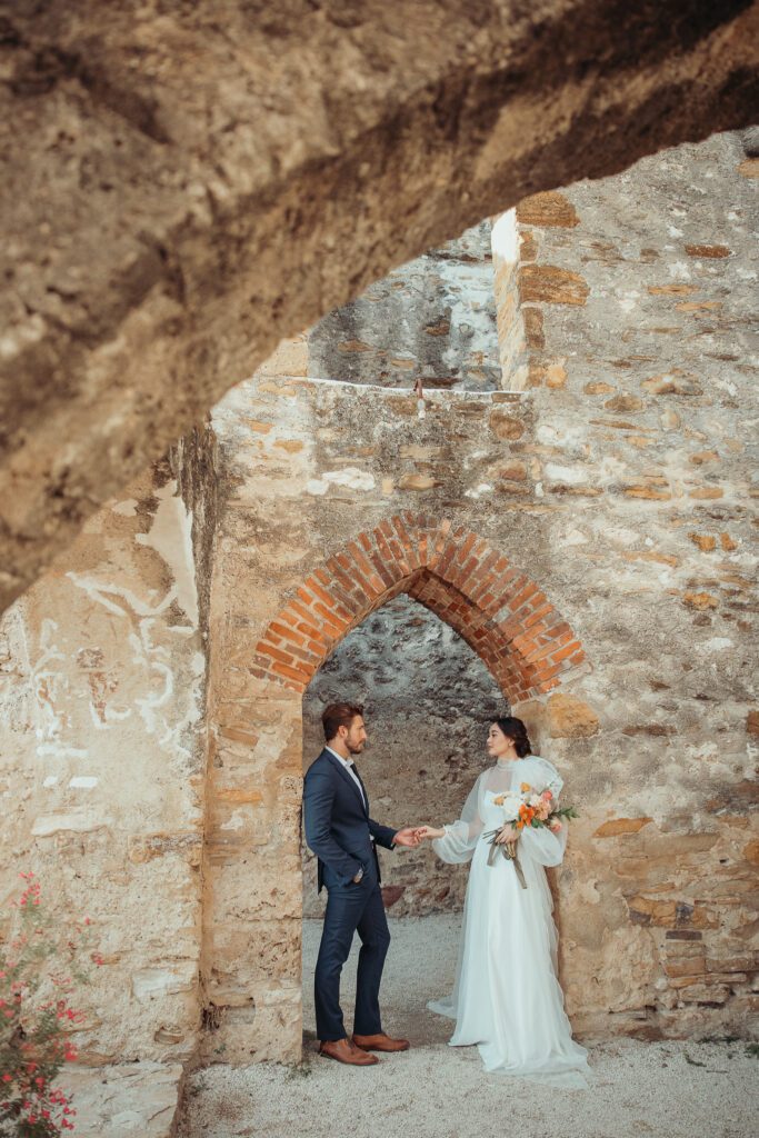 A bride and groom holding hands under a stone archway in The Missions in San Antonio. 