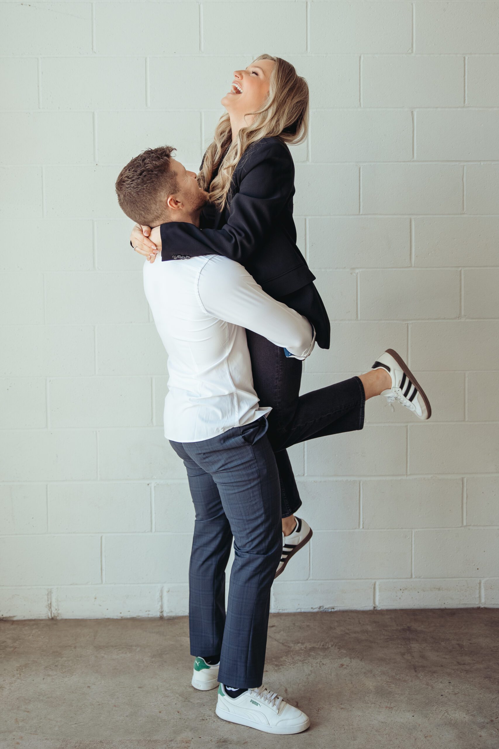 Bride jumping into groom's arms during their studio session in Columbus, Ohio. Bride is wearing a black blazer and groom is in blue pants and a white shirt.