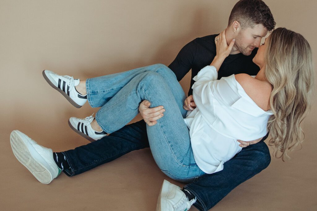 Bride sitting in groom's lap on the floor being dipped back being playful in a candid moment in a Columbus, Ohio studio during their engagement session.