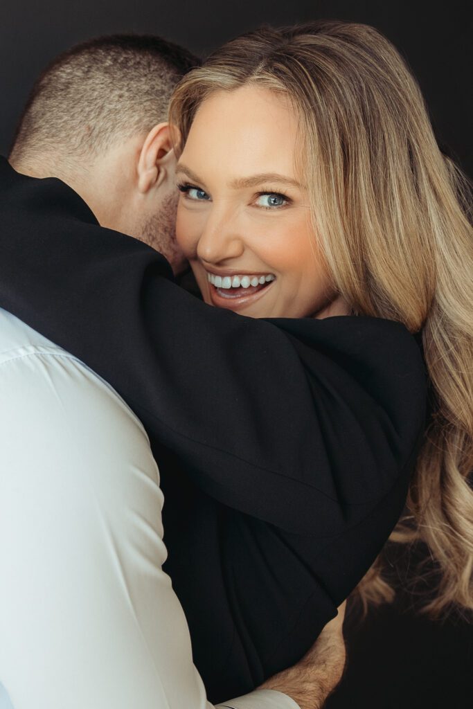 Bride and groom are hugging with the groom's face away from the camera while the bride is looking at the camera and smiling.